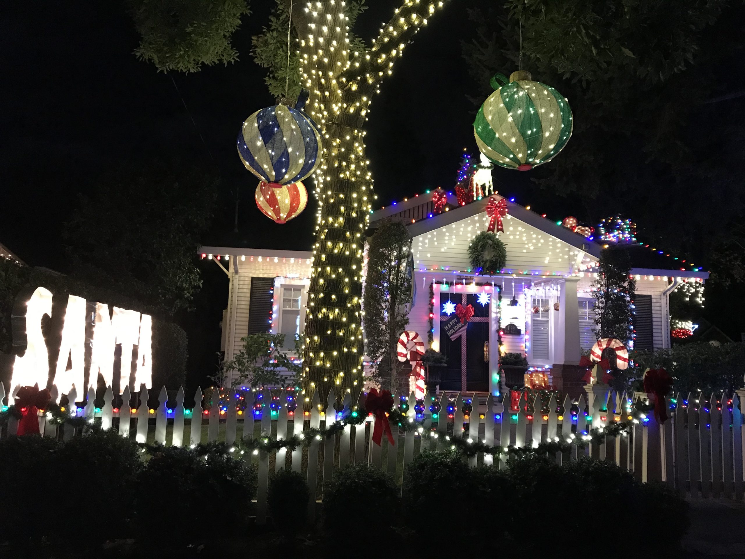 1 story home with a big tree in front yard and fence in front, covered in Christmas lights