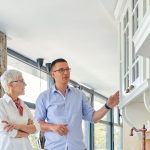 Prospective homebuyer and real estate professional examining kitchen cabinetry during a home tour before making an offer.
