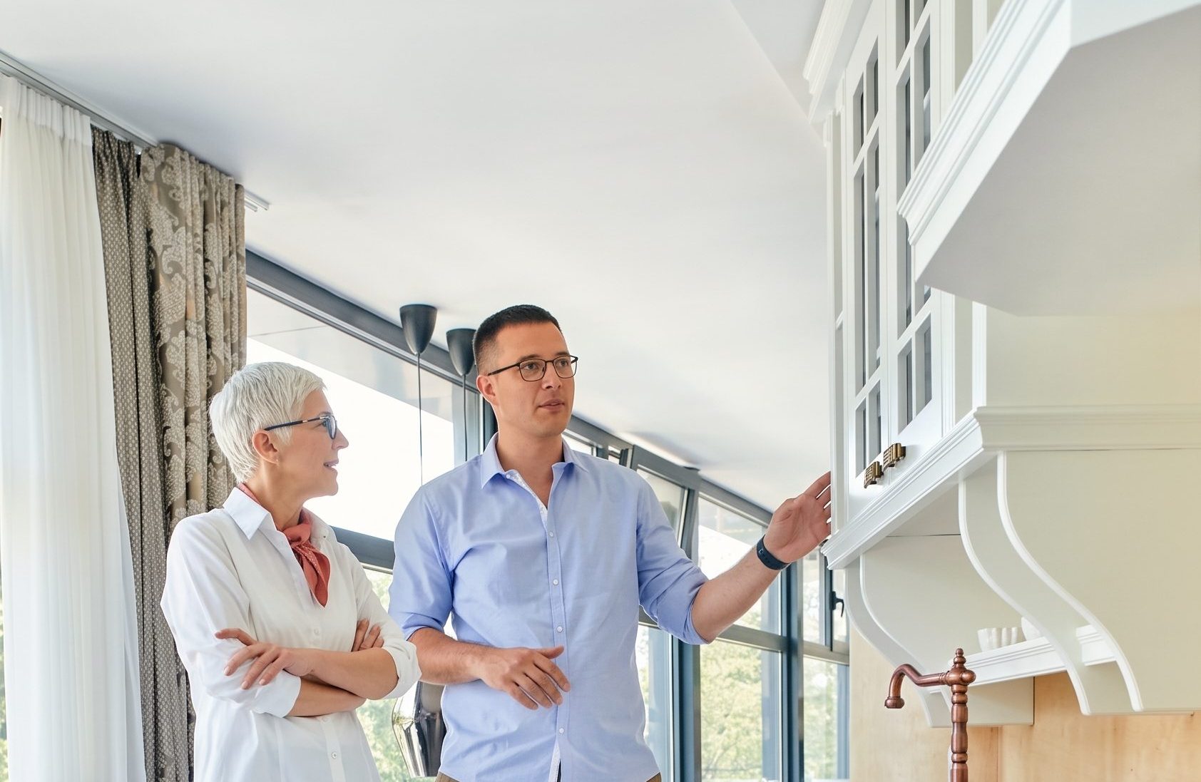 Prospective homebuyer and real estate professional examining kitchen cabinetry during a home tour before making an offer.