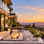 Modern luxury hillside home featuring floor-to-ceiling windows, outdoor terrace, fire pit, and panoramic sunset views.