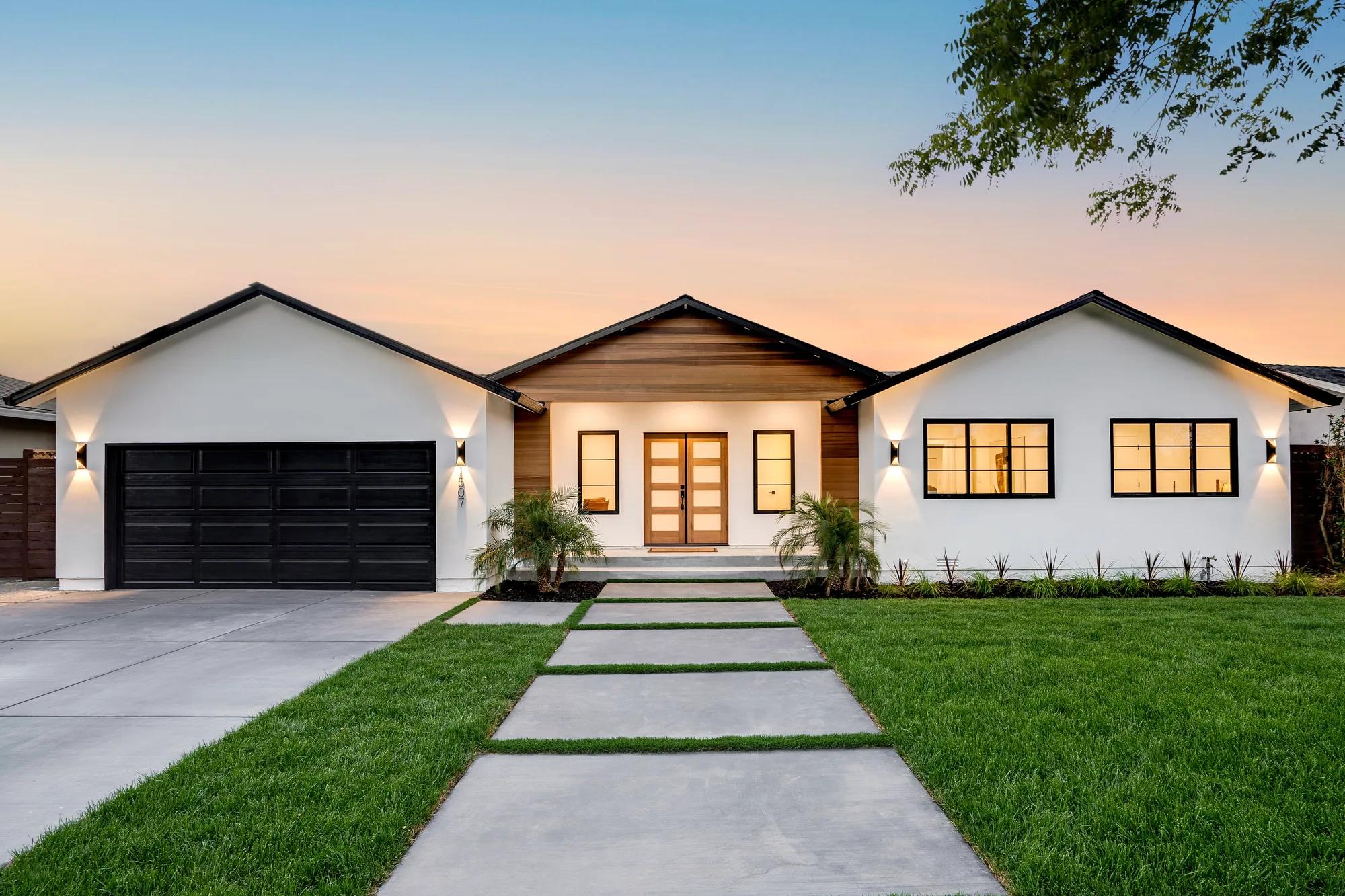 Willow Glen-style home with white exterior, dark garage door, mature trees, and landscaped front yard in warm evening light.